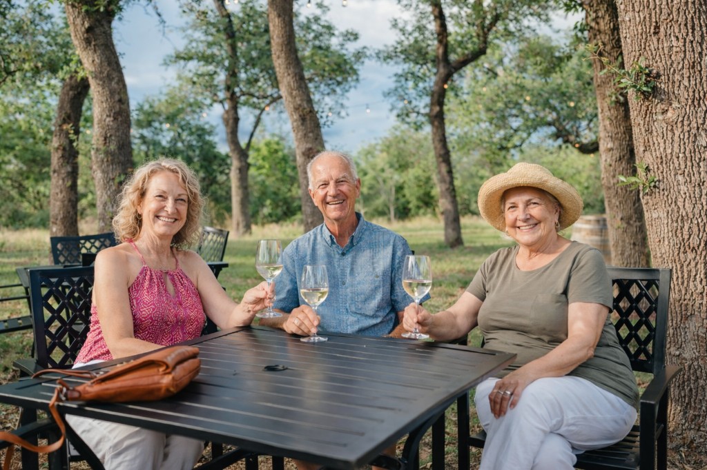 Three guests with wine at an outdoor table under the trees